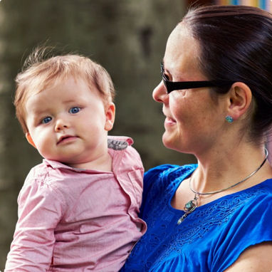 A mother looking at her baby which she is holding who is looking towards the camera.
