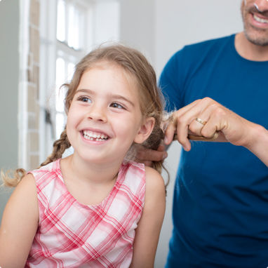 A father happily doing his daughters hair for her.
