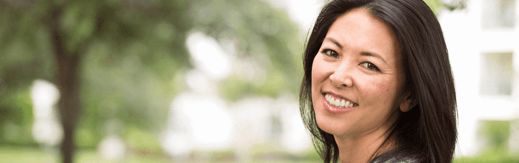 A smiling woman leaning against an indoor wall.