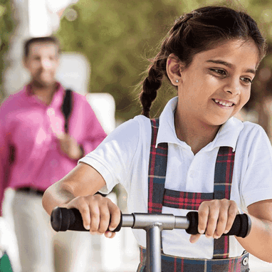 A young girl riding around on her pink, three wheeled scooter.