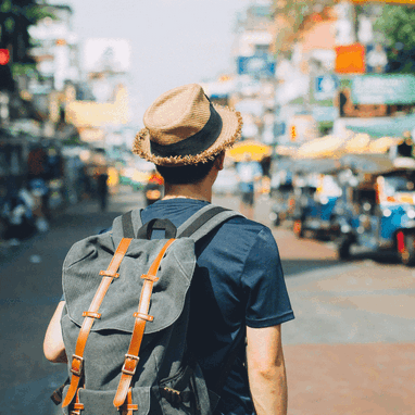 A traveler walking through a busy Asian street wearing a fedora.