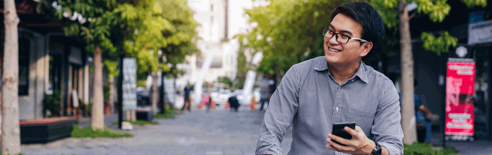A young man standing and smiling in an urban setting.