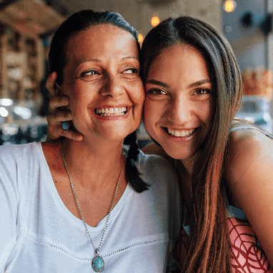 Two young women laughing and embracing in front of a sunny coastal scene. Two young women laughing and embracing in front of a sunny coastal scene.