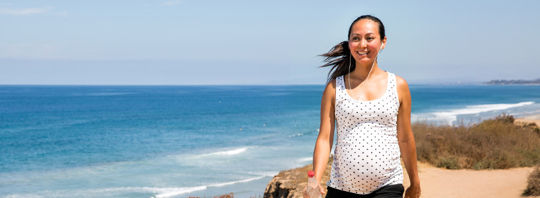 A pregnant woman happily walking down a sunny beach. A pregnant woman happily walking down a sunny beach.