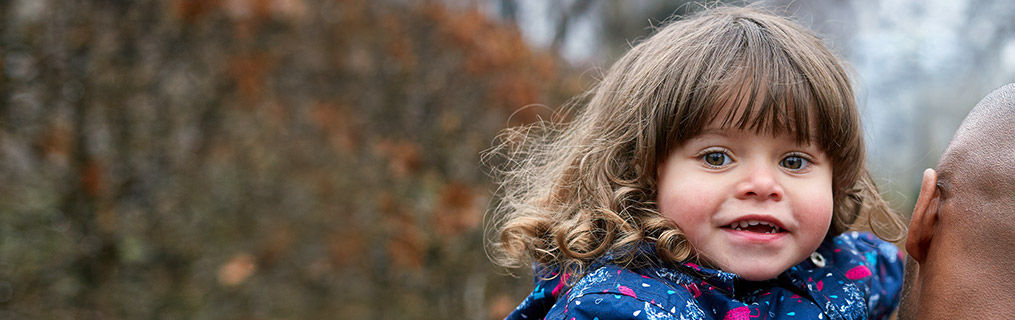 A smiling long haired child looking to the camera being carried by a man.
