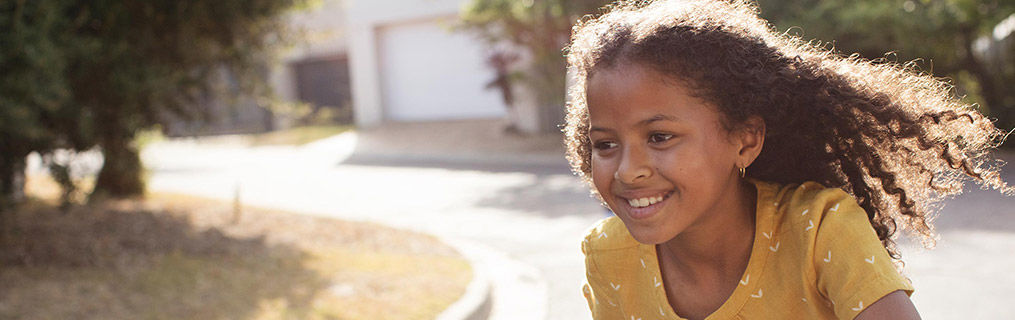 A young girl playing outdoors in a sunny street.