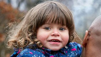 A smiling long haired child looking to the camera being carried by a man. A smiling long haired child looking to the camera being carried by a man.