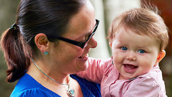 A smiling and happy baby looking to the camera in the arms of its mother. A smiling and happy baby looking to the camera in the arms of its mother.