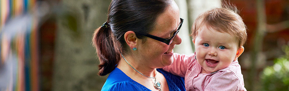 A smiling and happy baby looking to the camera in the arms of its mother.
