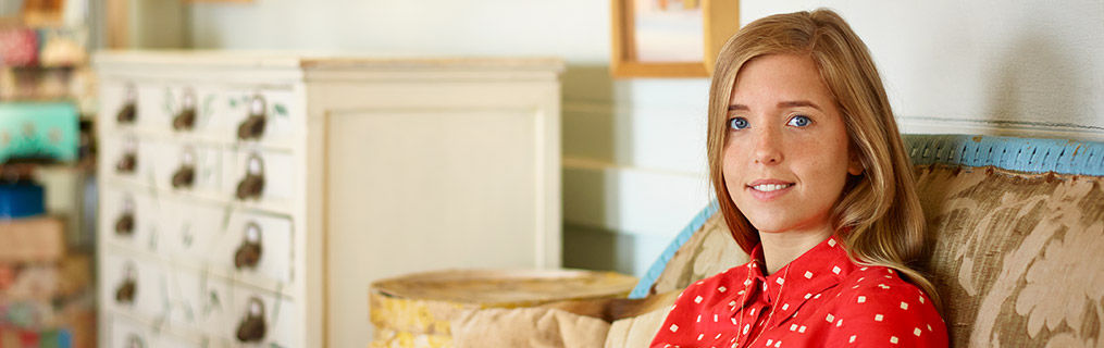 An adolescent young woman sitting in her living room smiling.