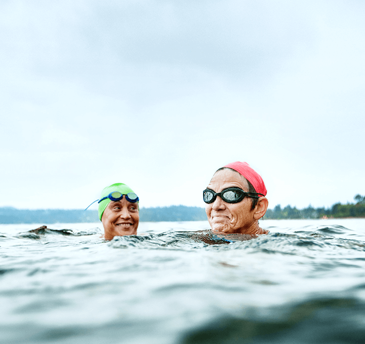A man and woman in the ocean wearing googles and colourful swimming caps