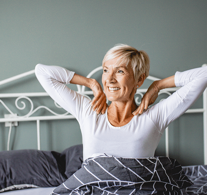 A smiling woman stretching after waking up in bed
