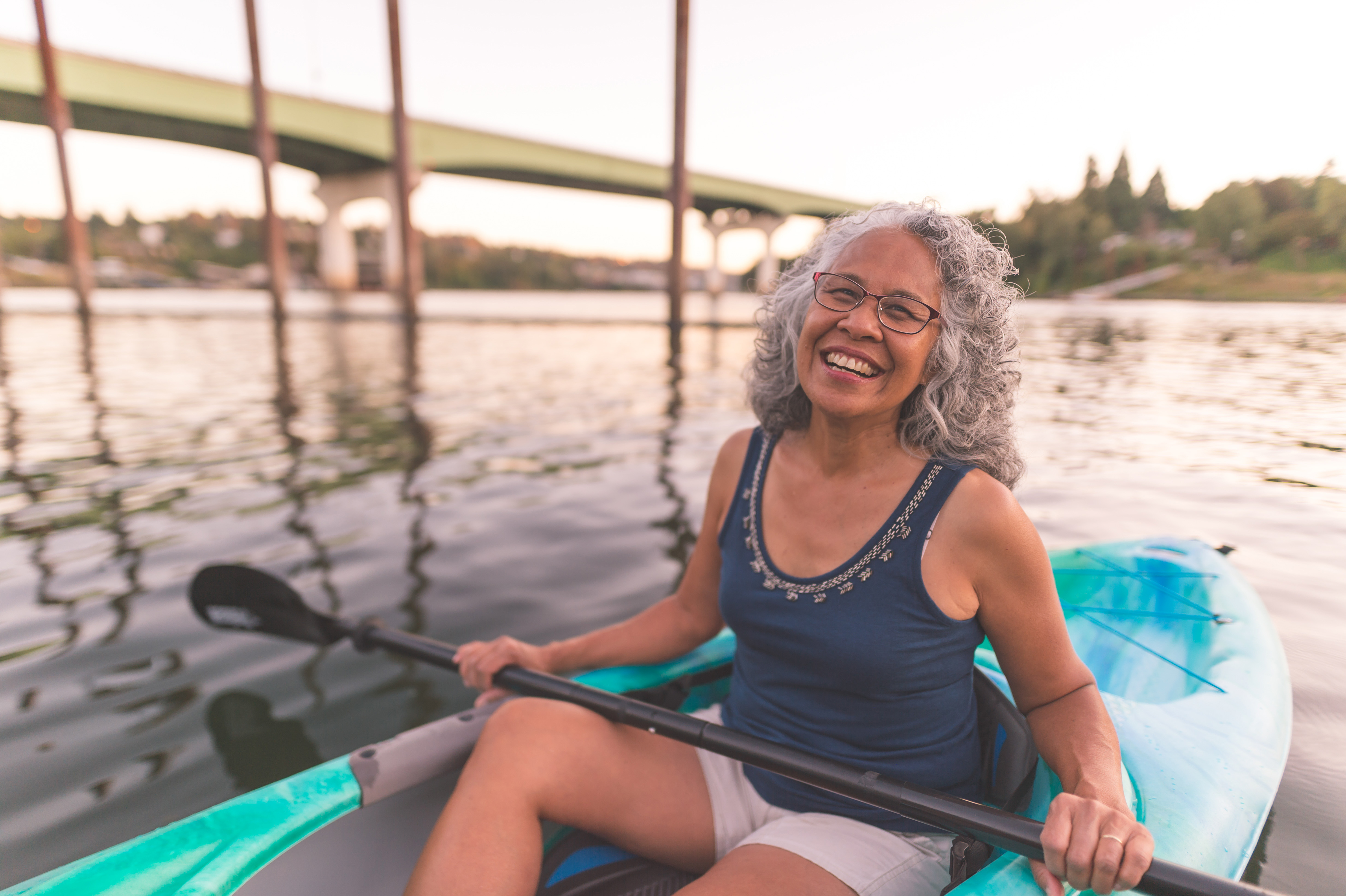 A smiling woman sitting in a kayak holding a paddle with both hands