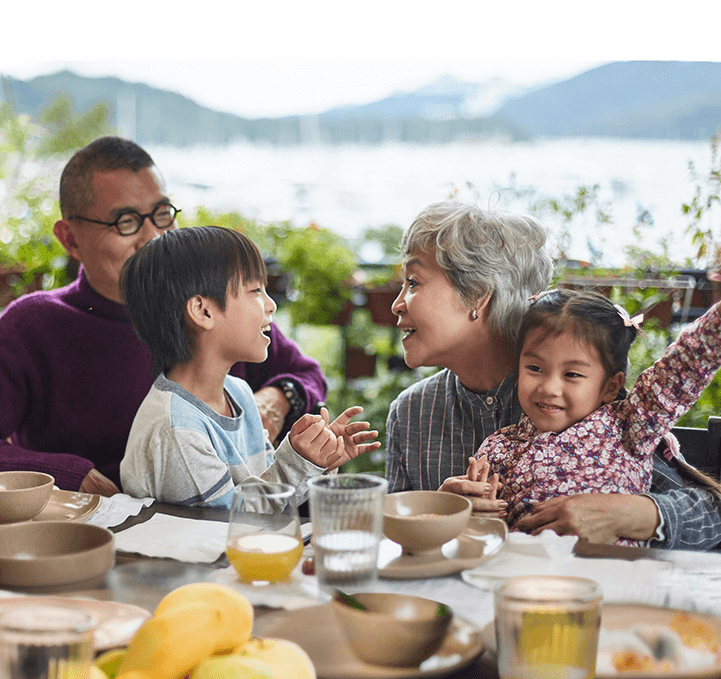 Two grandparents sitting at a dining table and laughing with their grandkids sitting in their laps