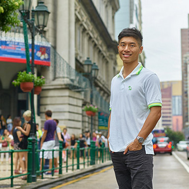 A young man sitting inside a glass ceilinged building smiling.