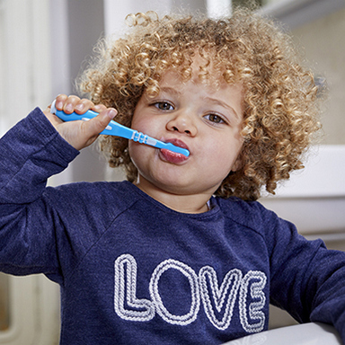 A young, curly haired boy brushing his teeth.