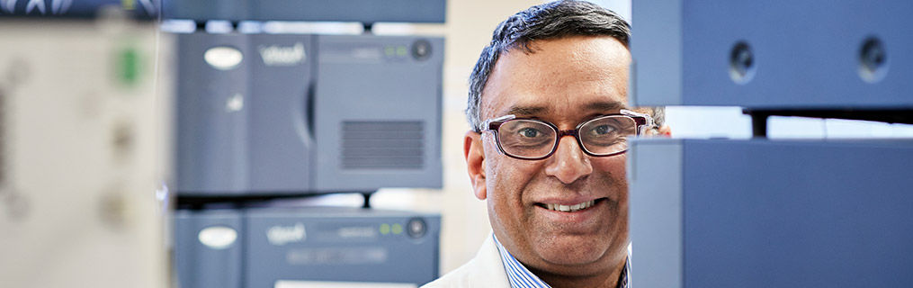 A middle aged scientist with glasses standing amongst research equipment.